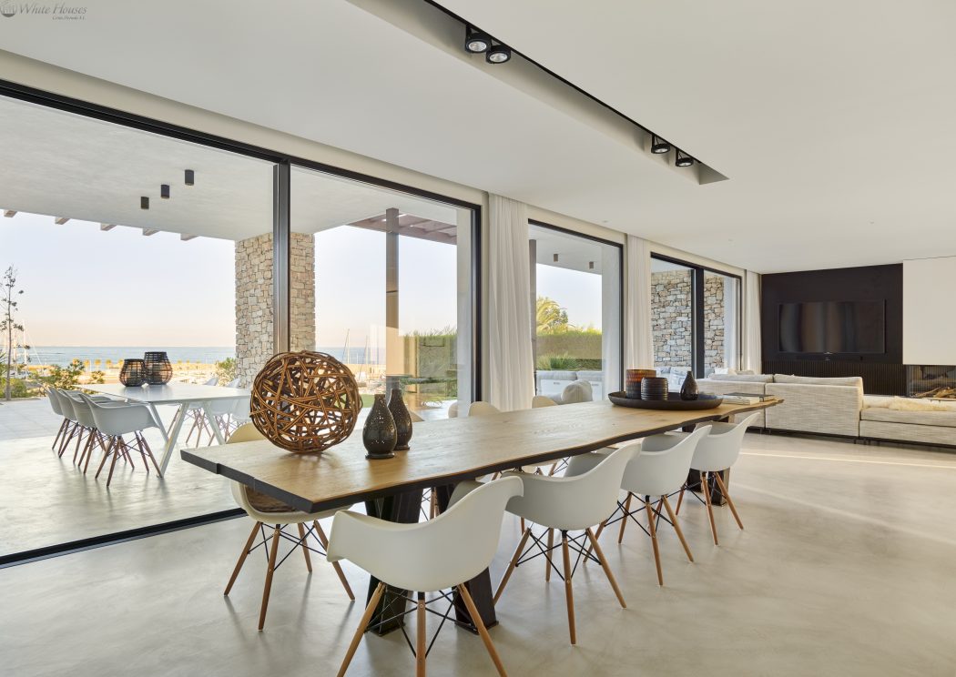 Sleek modern architectural design with large glass windows, wooden dining table, and contemporary decor.