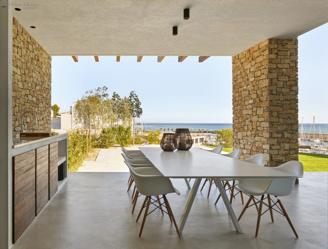 Minimalist outdoor dining space with stone walls, modern furniture, and ocean view.
