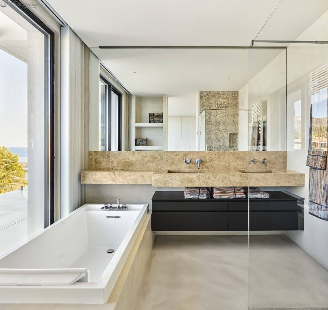 Modern bathroom with floor-to-ceiling windows, stone countertop, and sleek black vanity.