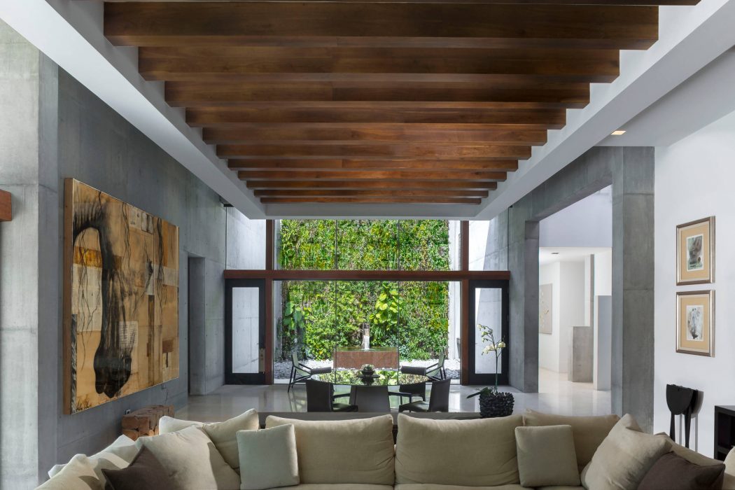 An open-concept living room with wooden beams and a large picture window overlooking greenery.