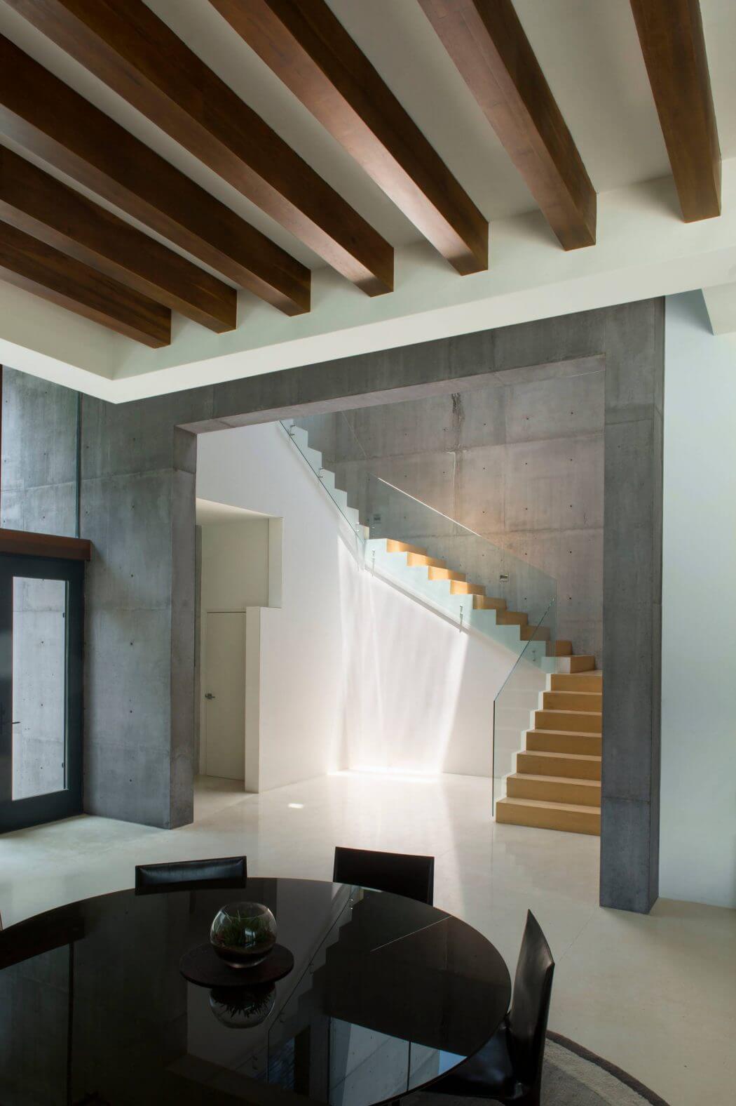 Elegant modern interior with concrete walls, wooden ceiling beams, and glass staircase.