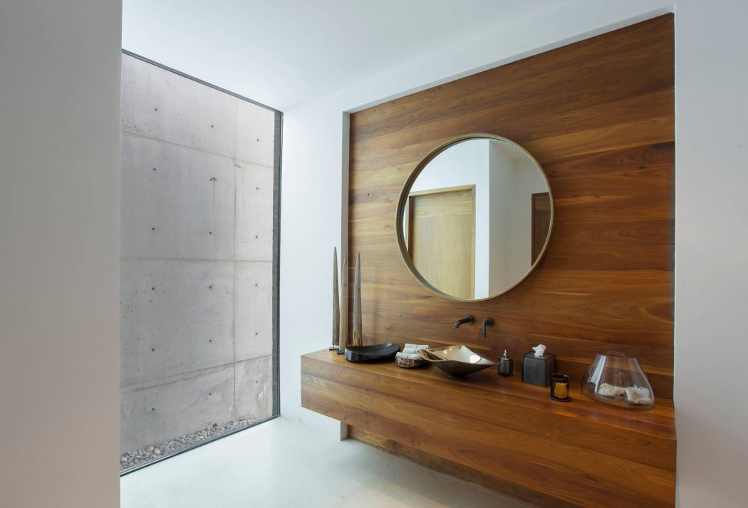 Minimalist bathroom design with concrete walls, wooden vanity, and round mirror.