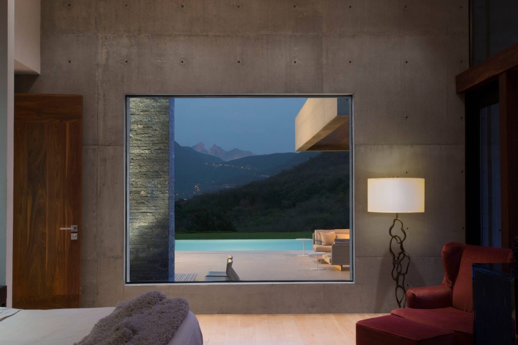 Spacious modern interior with concrete walls, large panoramic window framing mountain landscape.
