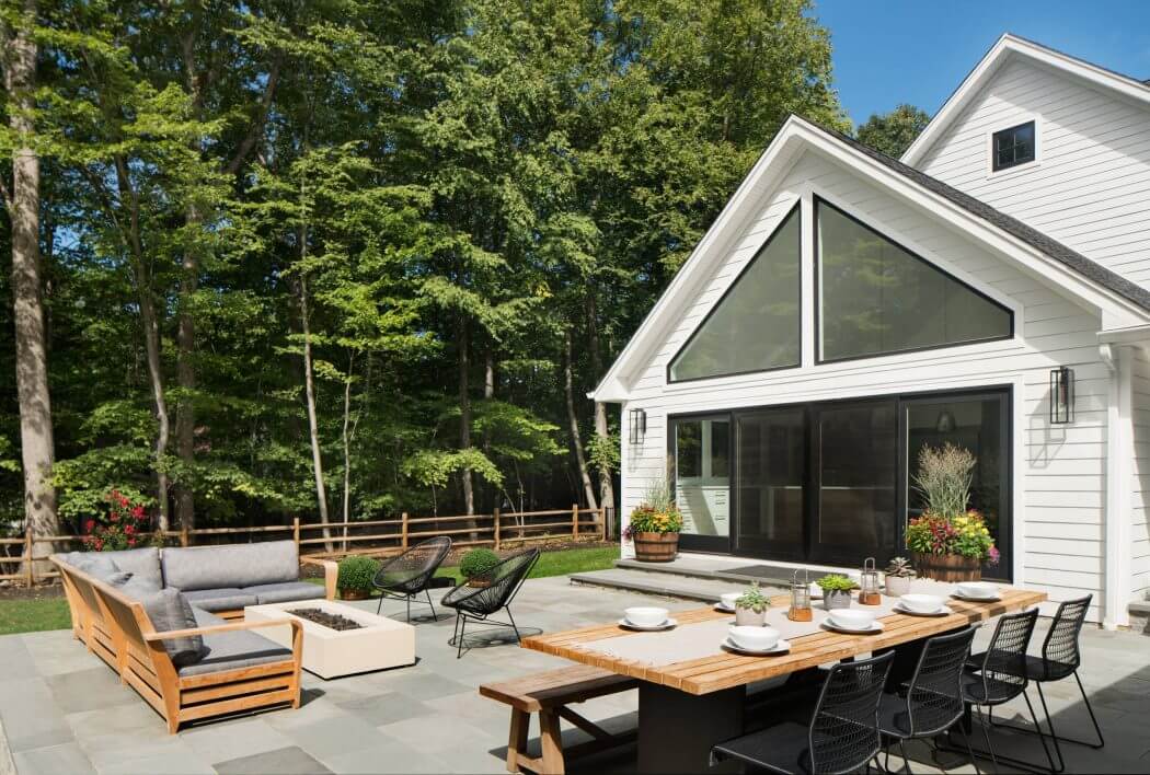 Spacious modern patio with wooden dining table, comfortable seating, and a wooded backdrop.