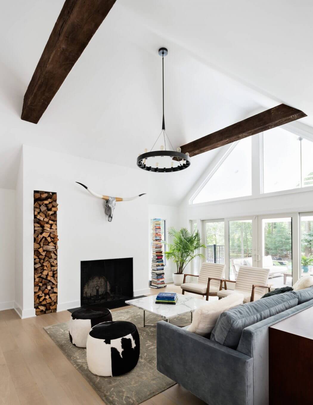 Spacious living room with high ceilings, exposed beams, and modern furniture. Fireplace and floor-to-ceiling windows.