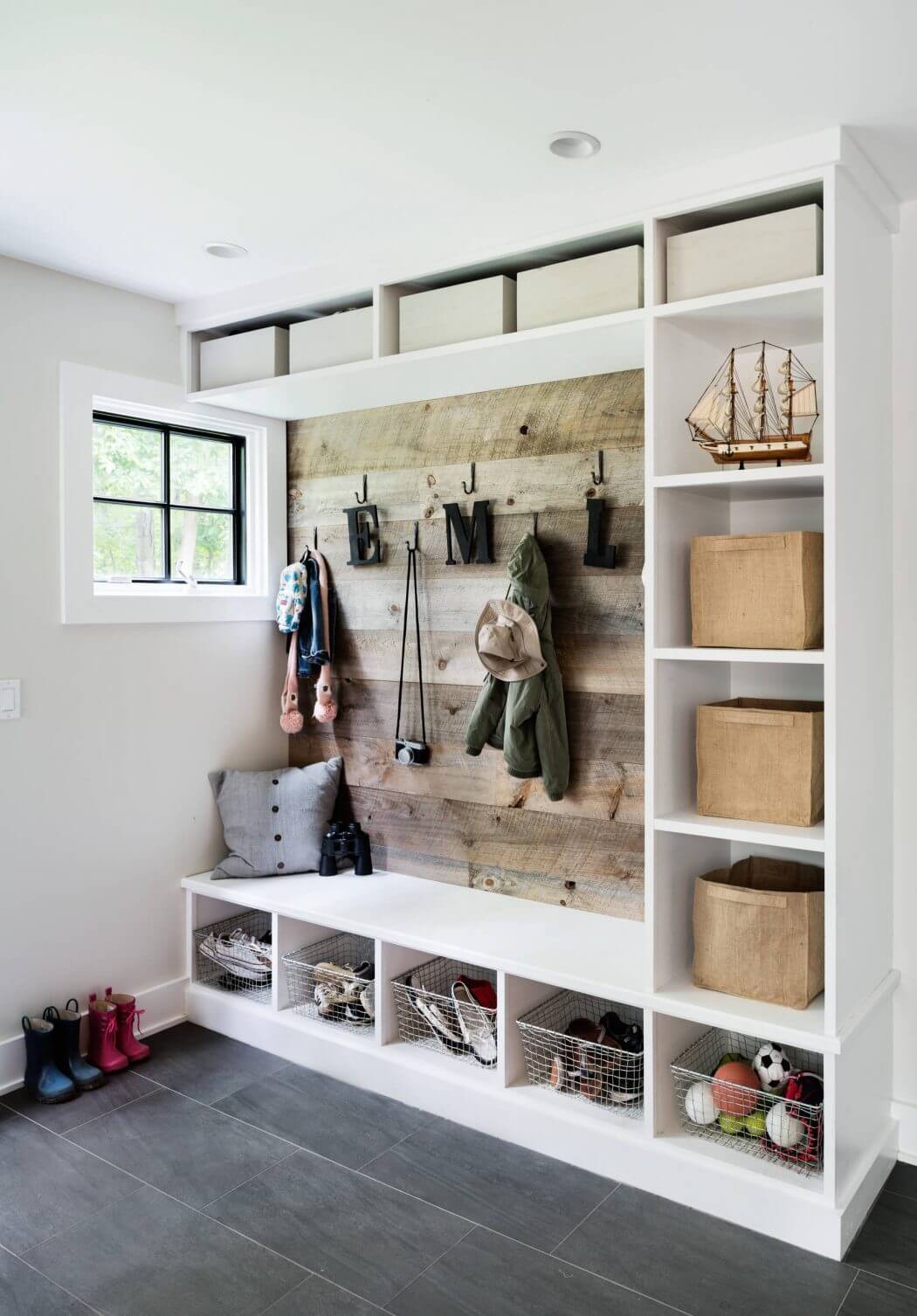 A modern mudroom with a rustic wood accent wall, built-in storage, and wire baskets.
