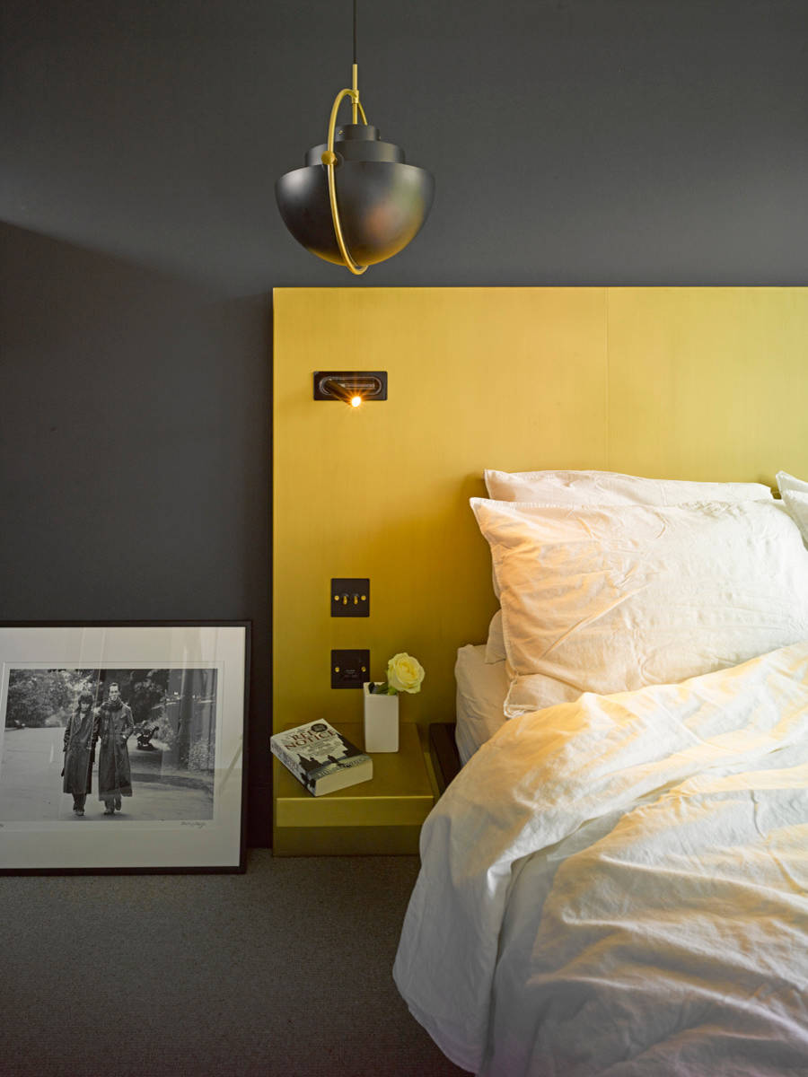 A cozy bedroom with a striking yellow accent wall, a pendant light, and a framed photograph.
