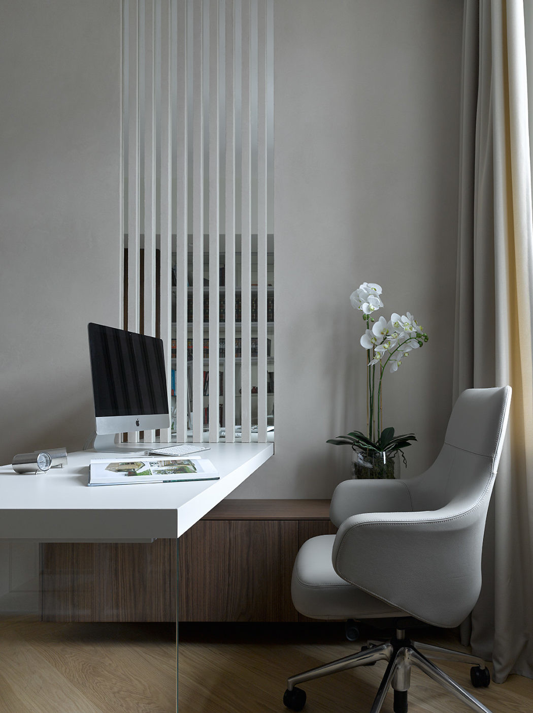 Minimalist home office with sleek desk and chair by a window with vertical blinds.