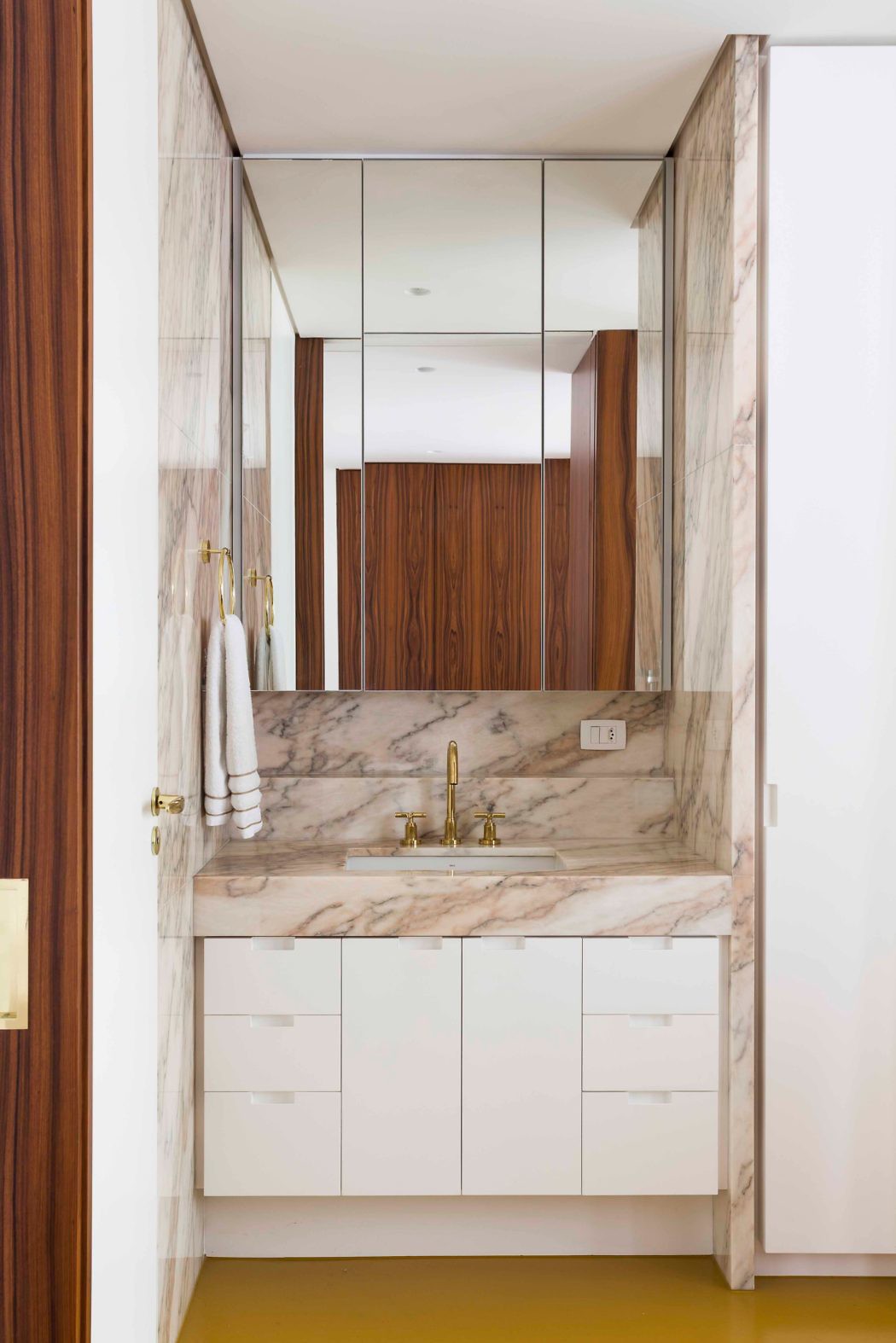 Modern bathroom with marble walls and white cabinetry.
