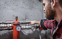 The man looks at the faucet, pipes, valve, pressure meter.