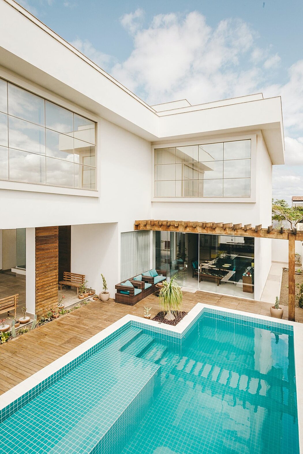 Modern two-story white house with large windows overlooking a blue swimming pool.