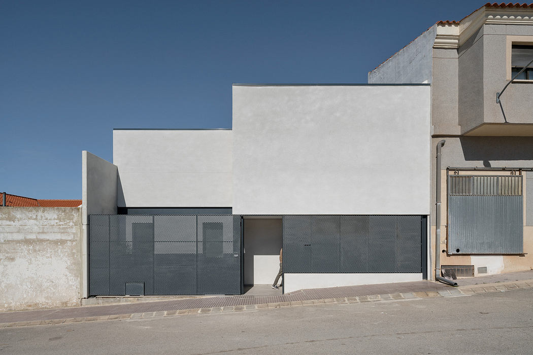 Modern minimalist building with a flat facade and garage doors beside traditional houses.