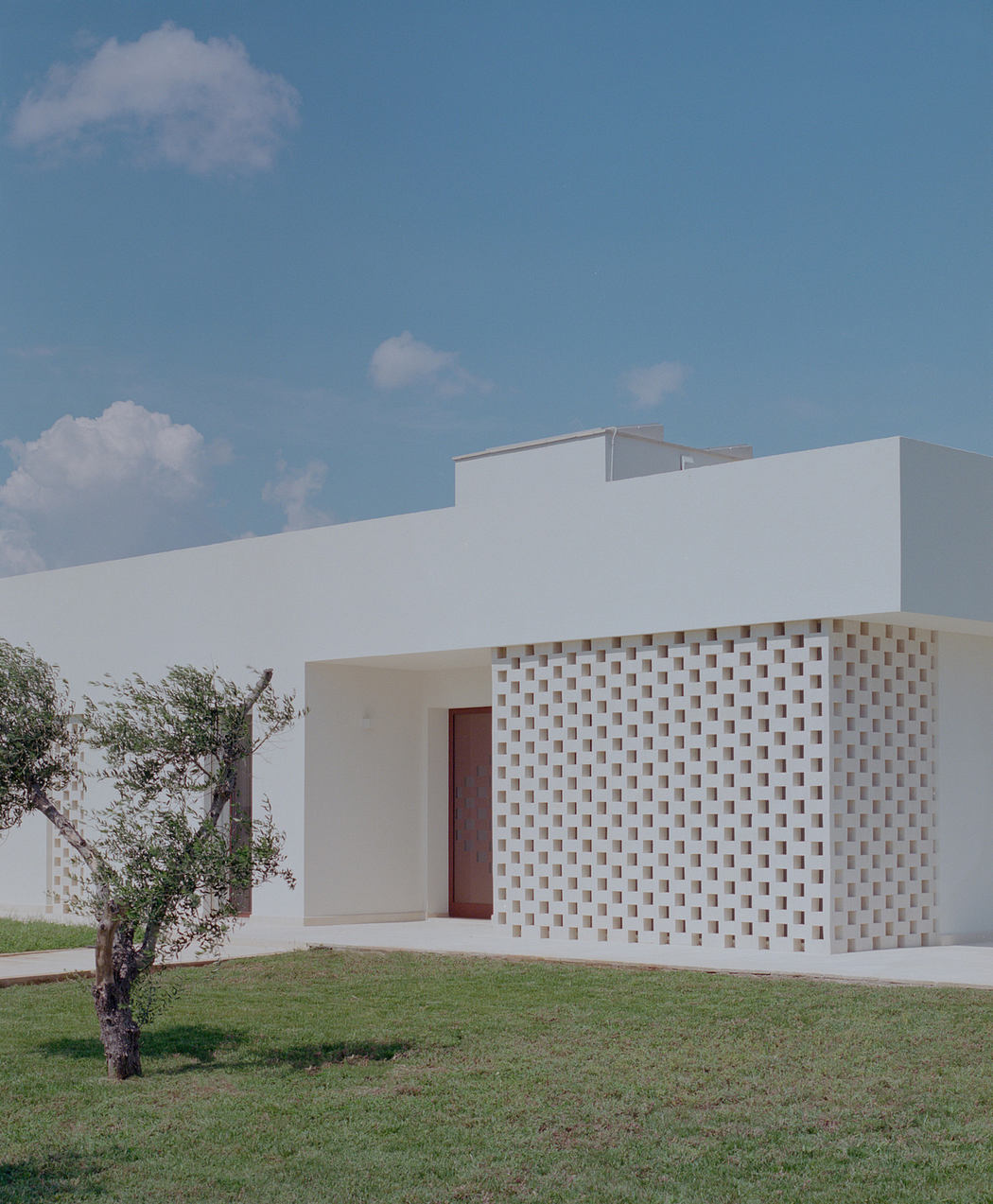 Modern white building with geometric lattice wall and red door.