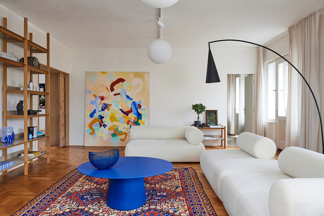Modern living room with large abstract painting, blue table, and white sofas.