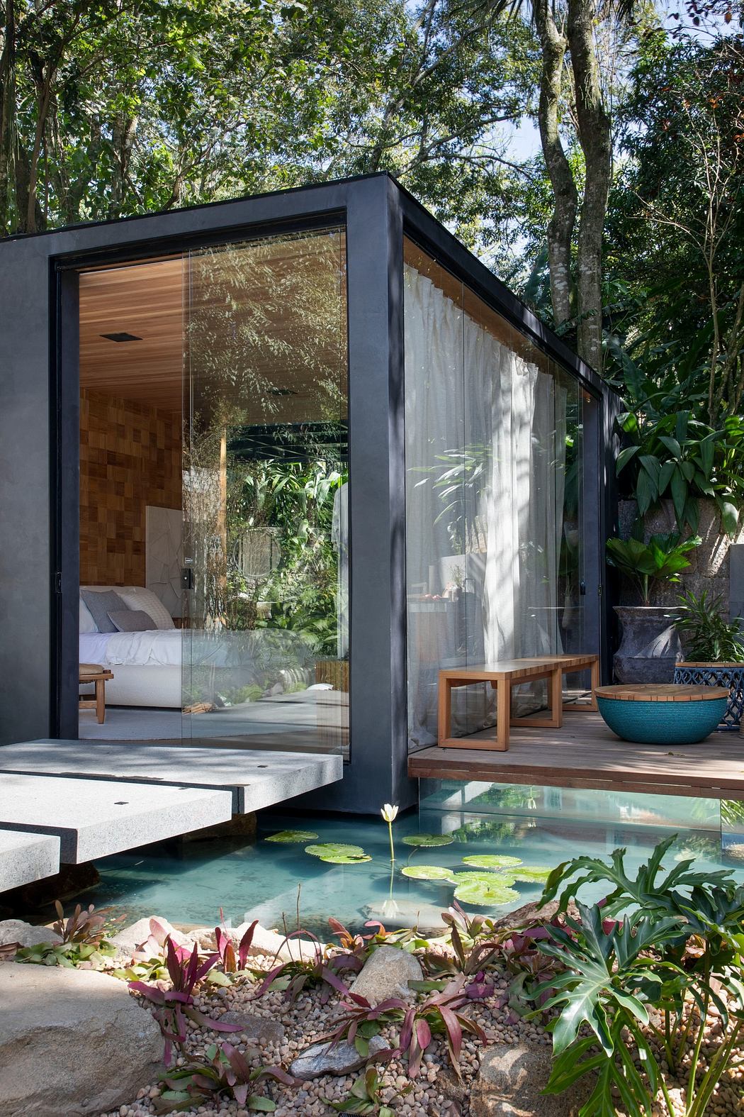 Modern glass-walled cabin with wooden interior, adjacent to a pond surrounded by green