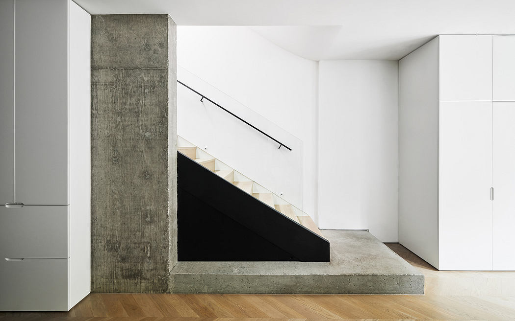 Minimalist interior with concrete staircase, white walls, and wooden floor.