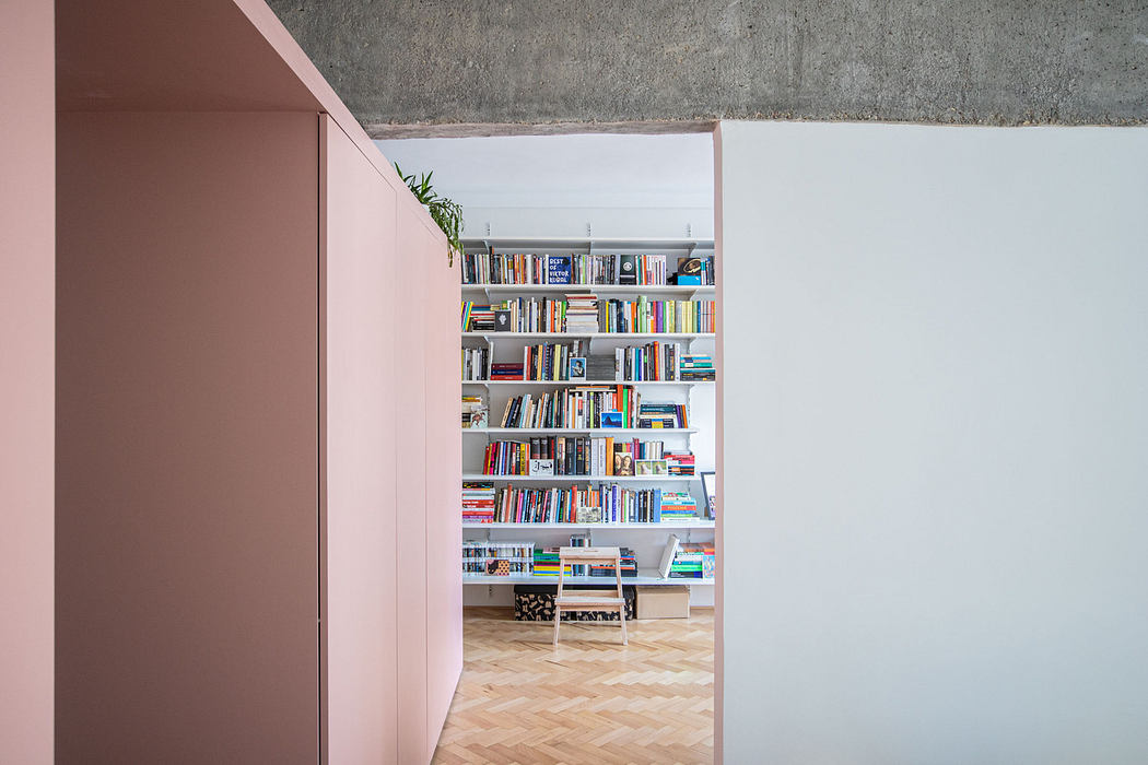 Modern room with pink wall and extensive bookshelf visible through doorway.
