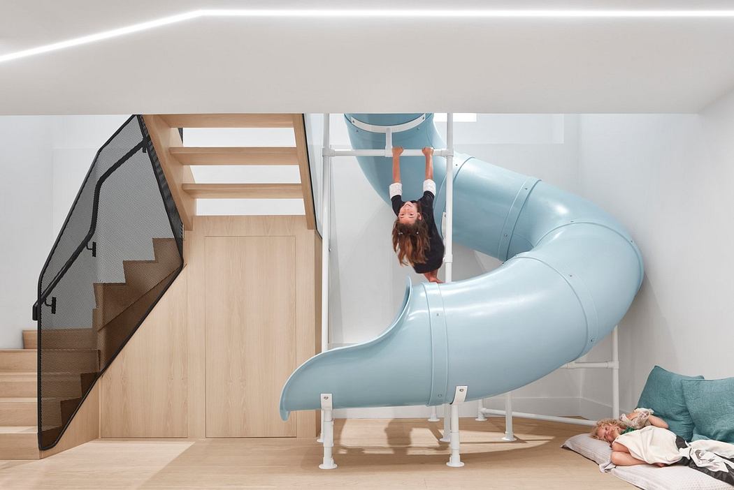 Modern room with a blue slide, staircase, and person sliding down.