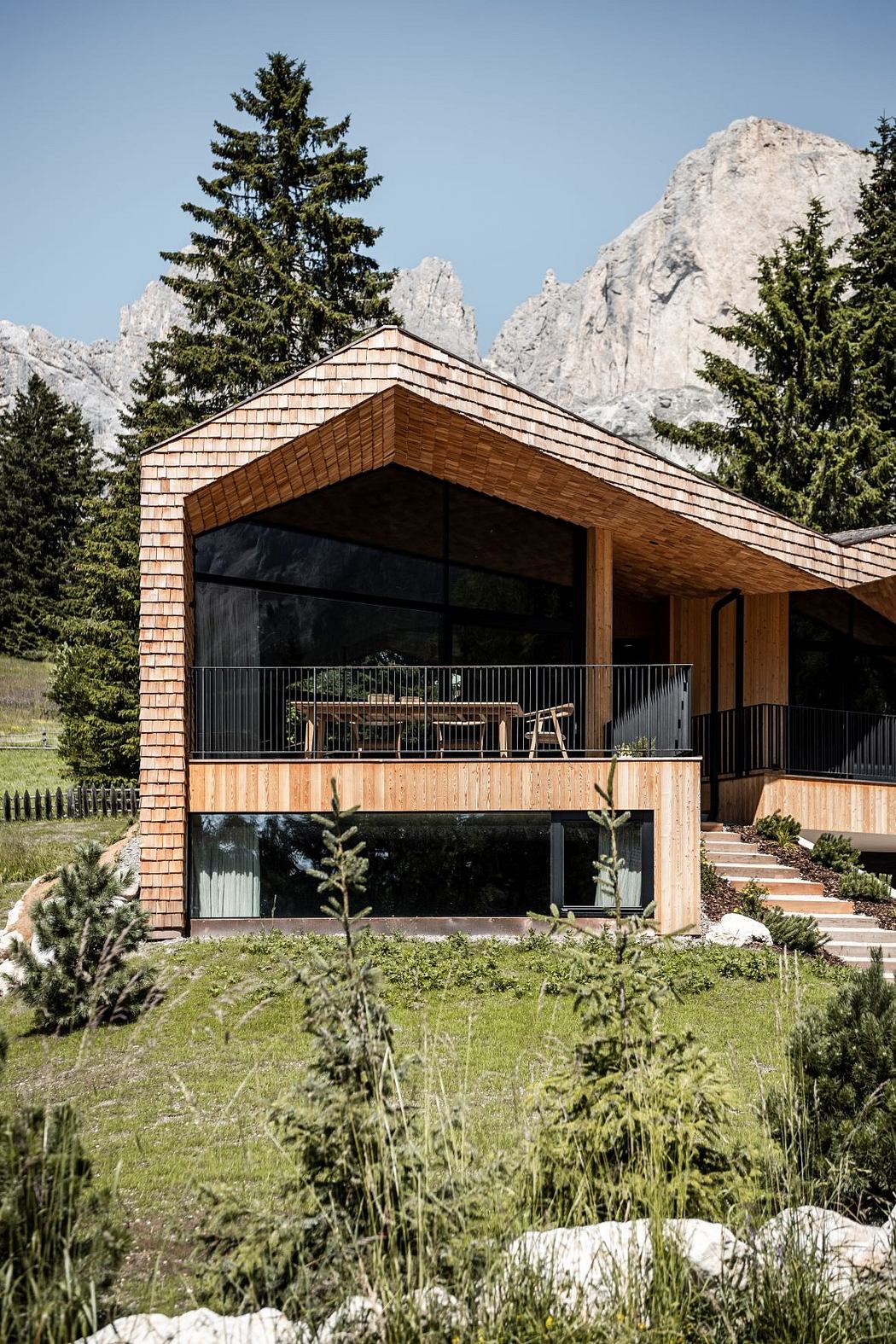 Modern wooden house with large windows against mountain backdrop.