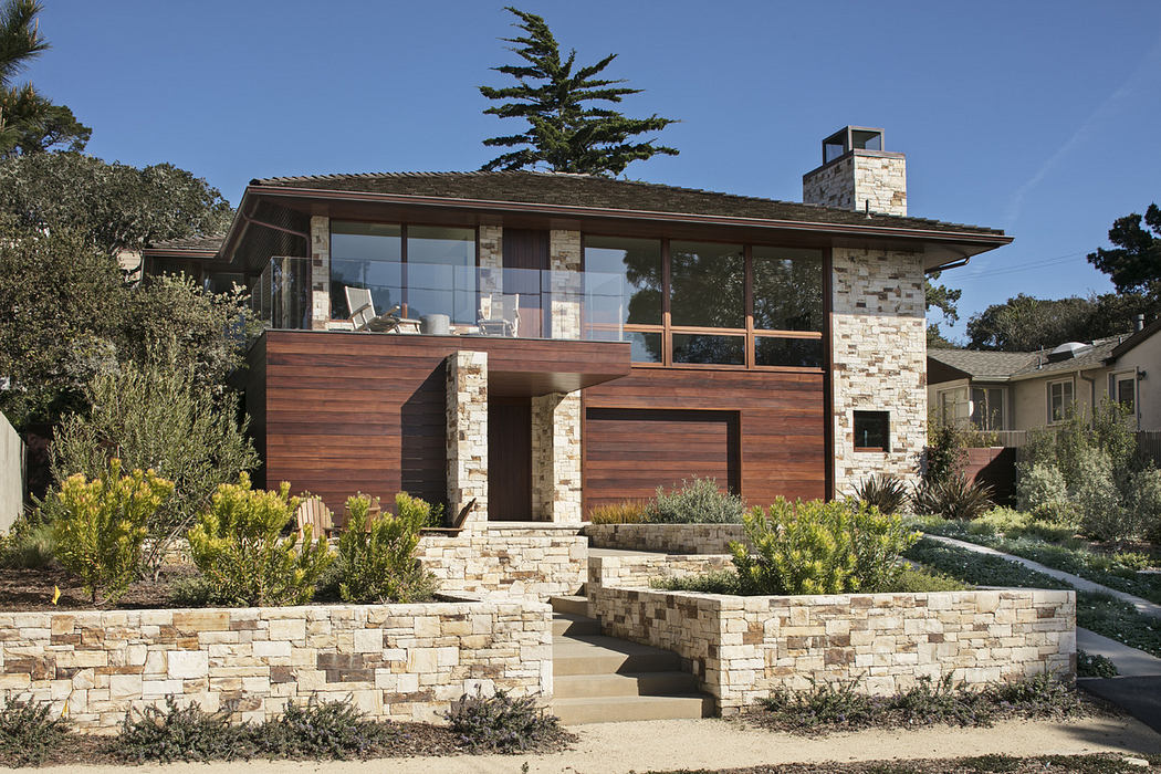Modern house with large windows, wooden siding, and stone foundation surrounded by greenery