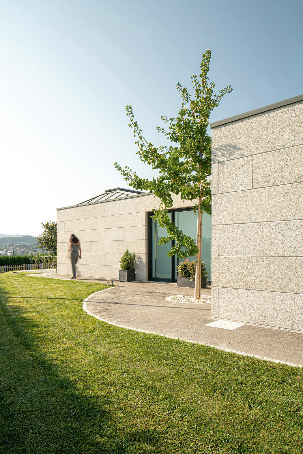 Modern building with textured walls, large windows, and a person approaching the entrance.