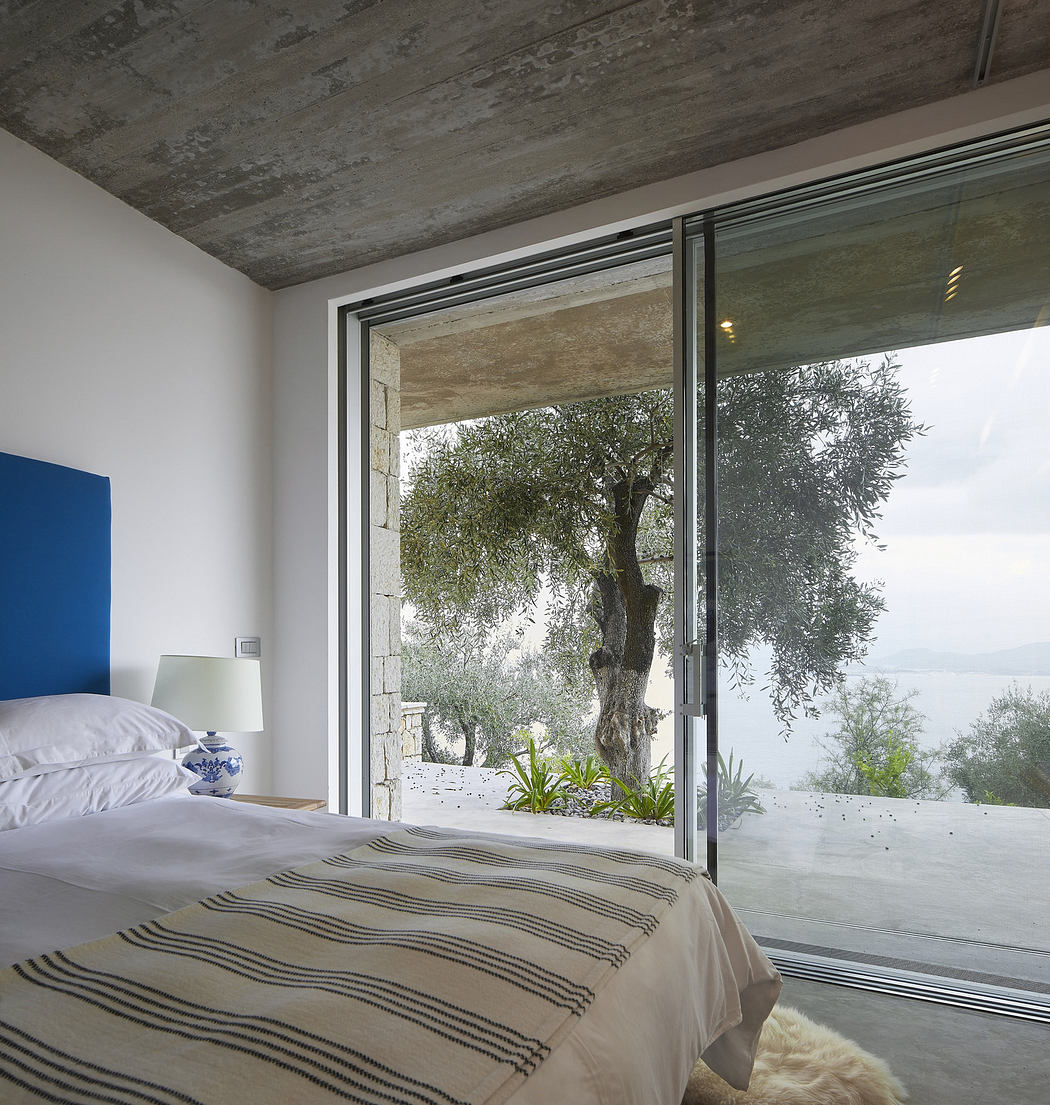Modern bedroom with large window overlooking a tree and lake.