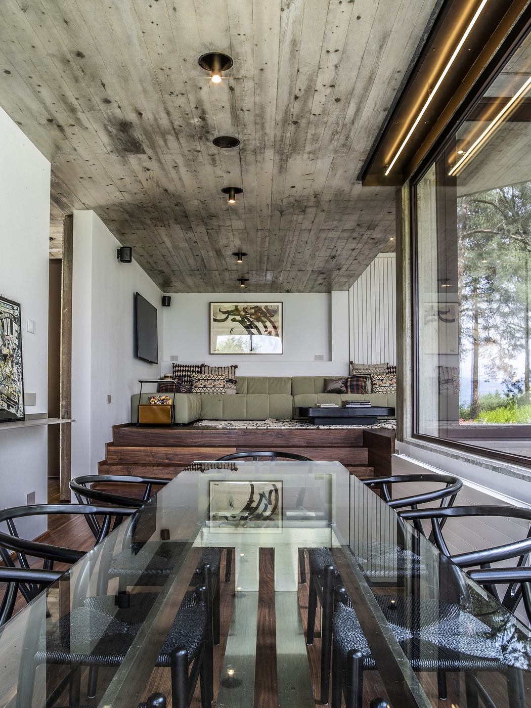 Modern dining room with glass table, concrete ceiling, and forest view.