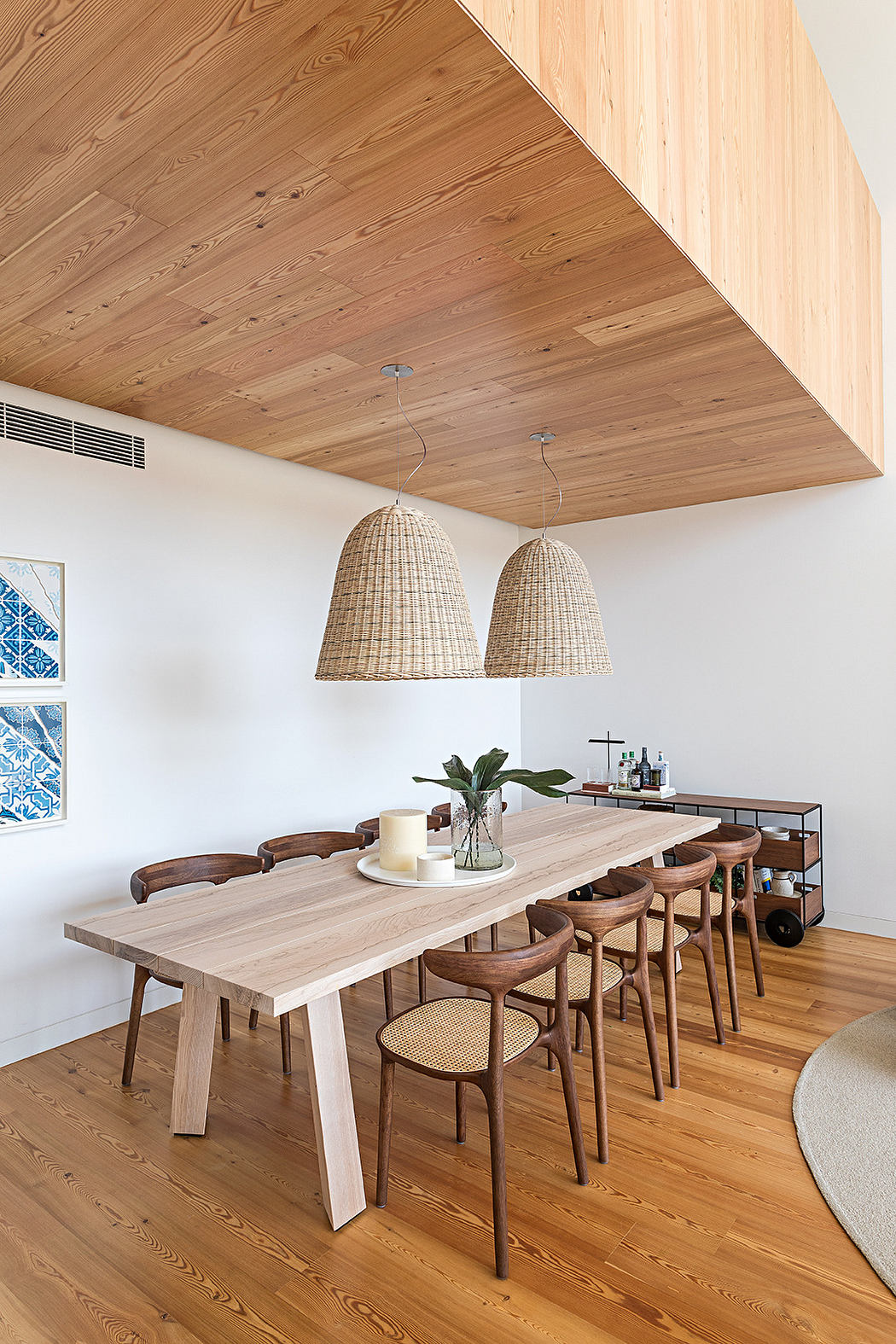 Modern dining room with wooden table, woven pendant lights, and slanted ceiling.