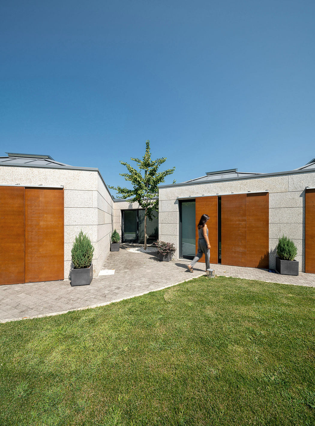 Modern courtyard with geometric design, green lawn, and a person walking.