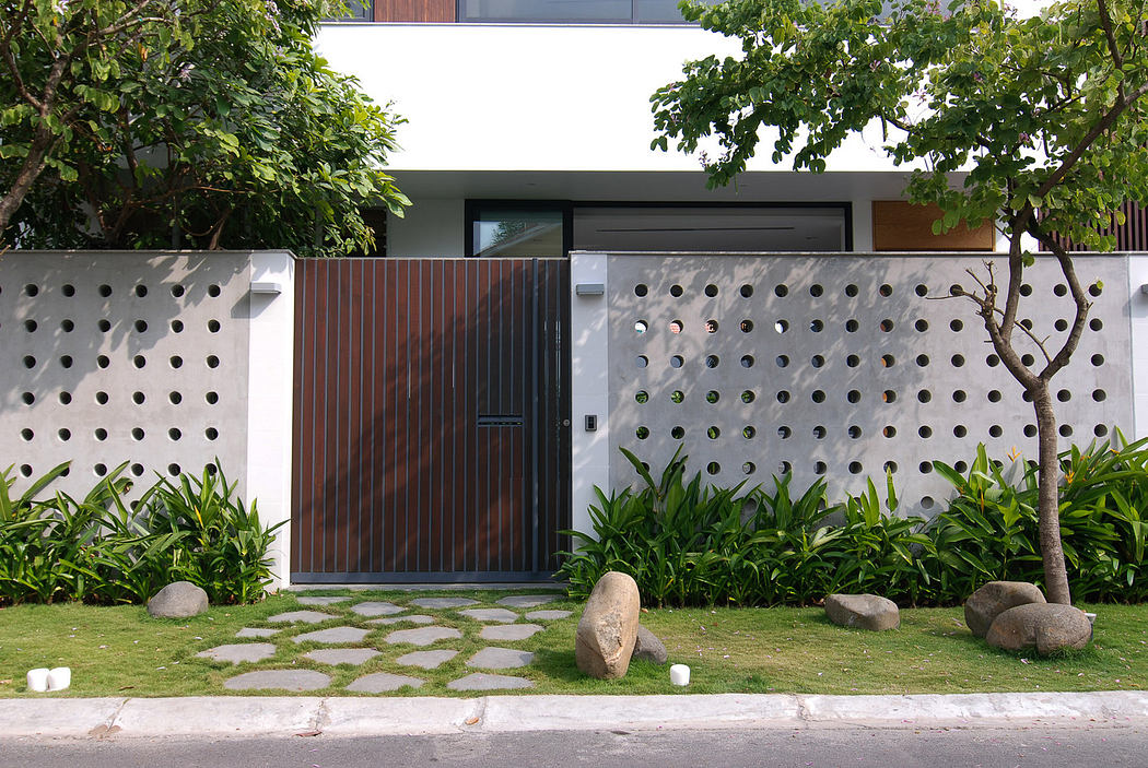 Modern house exterior with a decorative concrete wall and wooden gate, surrounded by greenery