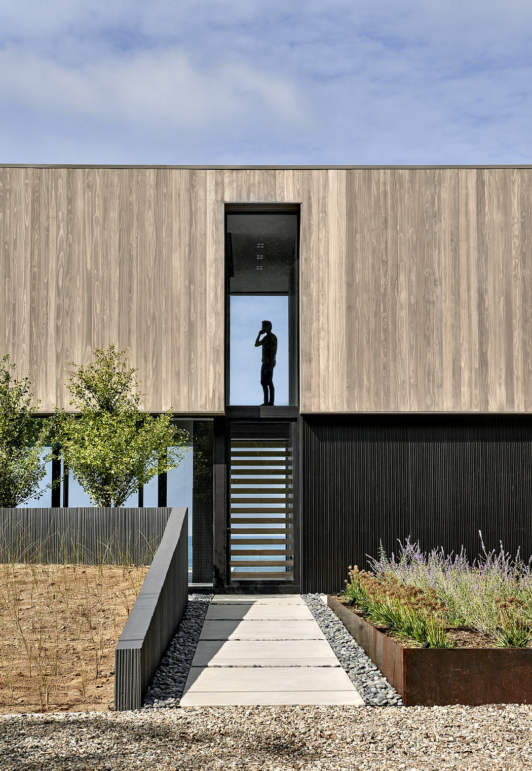 Modern house facade with wooden panels and a person at the entrance.