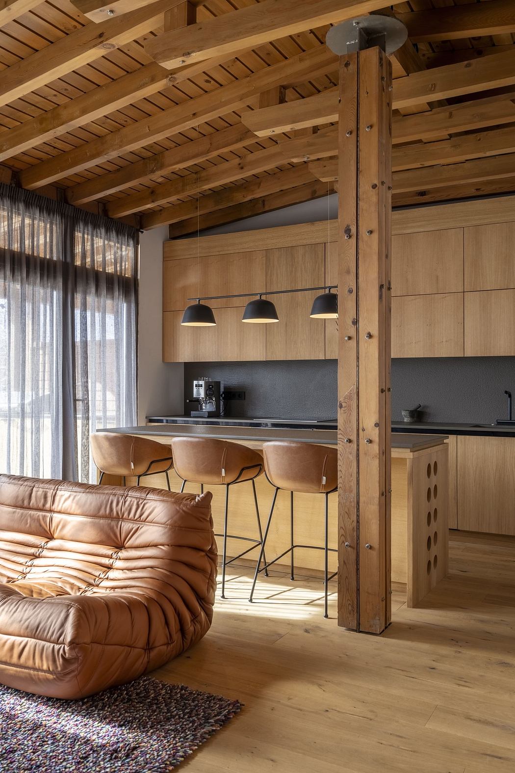 Modern kitchen with wood finish and bar stools, adjacent to a plush sofa.