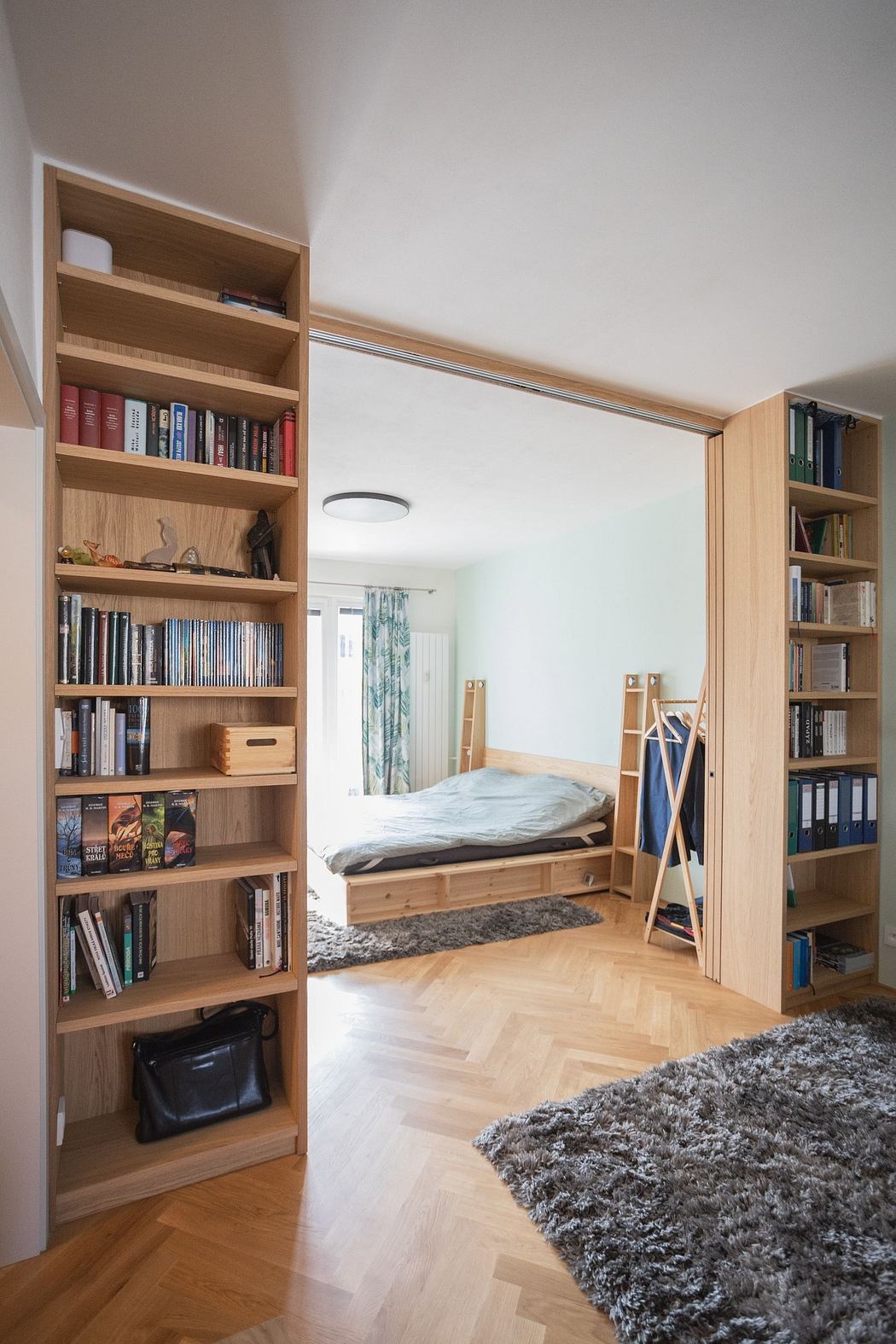 Modern bedroom with bookshelves, wood flooring, and a gray rug.