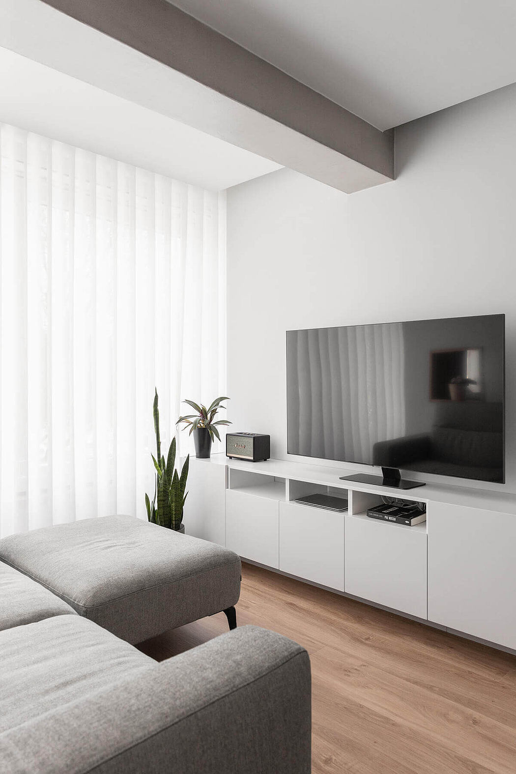 Minimalist living room with white media wall and sheer curtains.