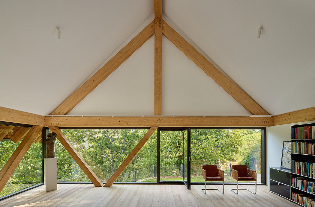 Modern attic room with exposed wooden beams and large windows overlooking nature.