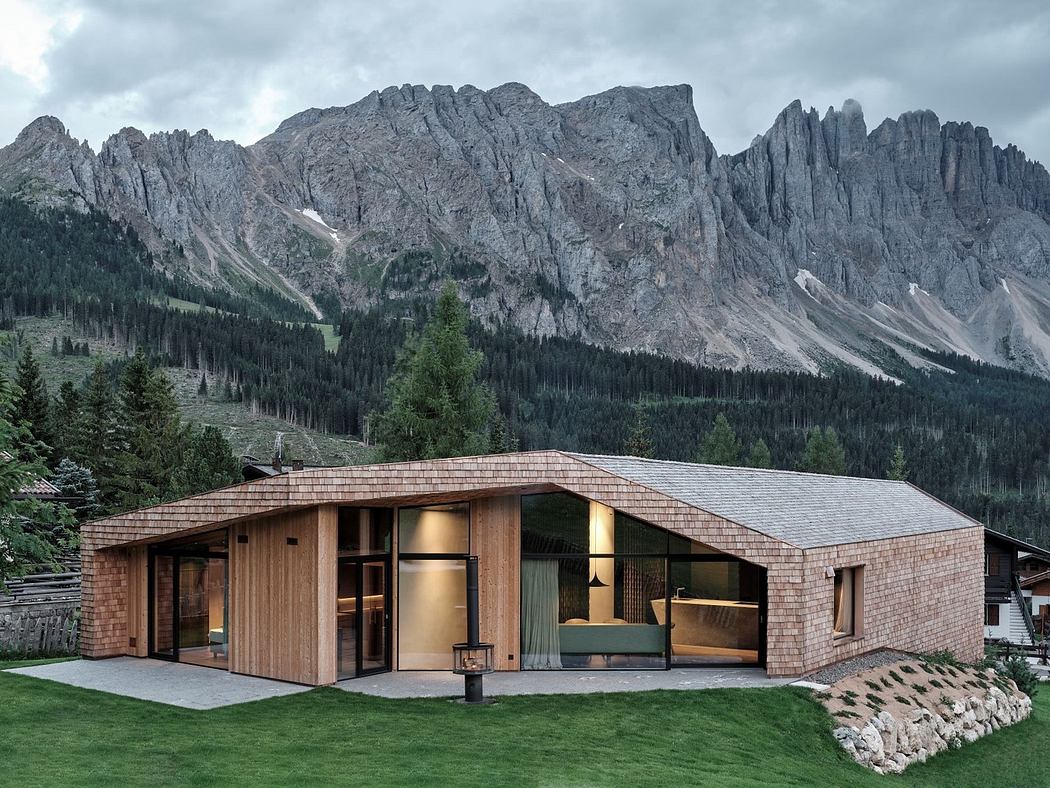 Modern mountain home with a pitched roof and large windows against a rugged mountain backdrop.