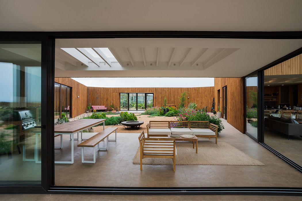 Modern courtyard with wooden benches and lush planters viewed through large glass windows.