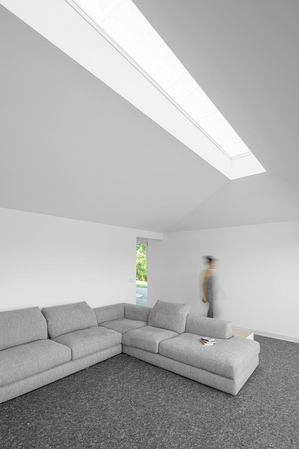 Minimalist interior with gray sectional sofa, white walls, skylight, and