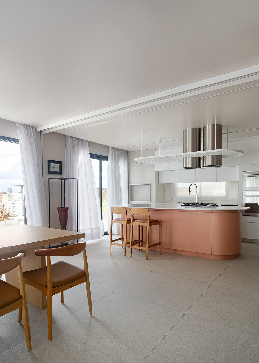 Modern kitchen with a pink island, wooden dining table, and light gray curtains.