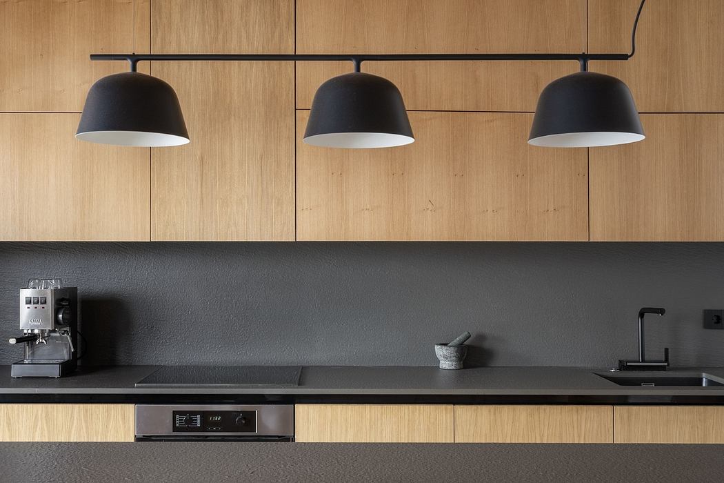 Modern kitchen with sleek wooden cabinets, pendant lighting, and black countertops.