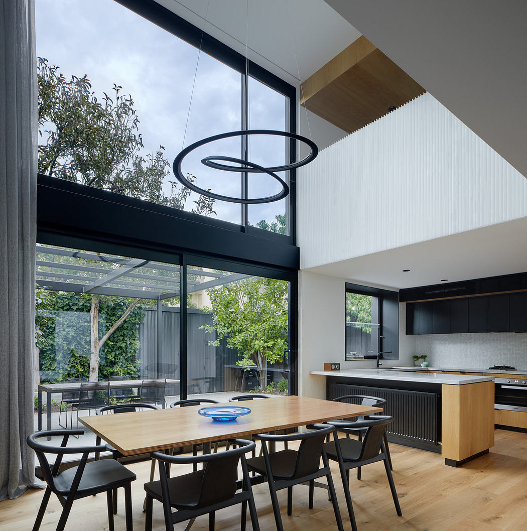 Modern kitchen with large windows, high ceiling, and a dining area.
