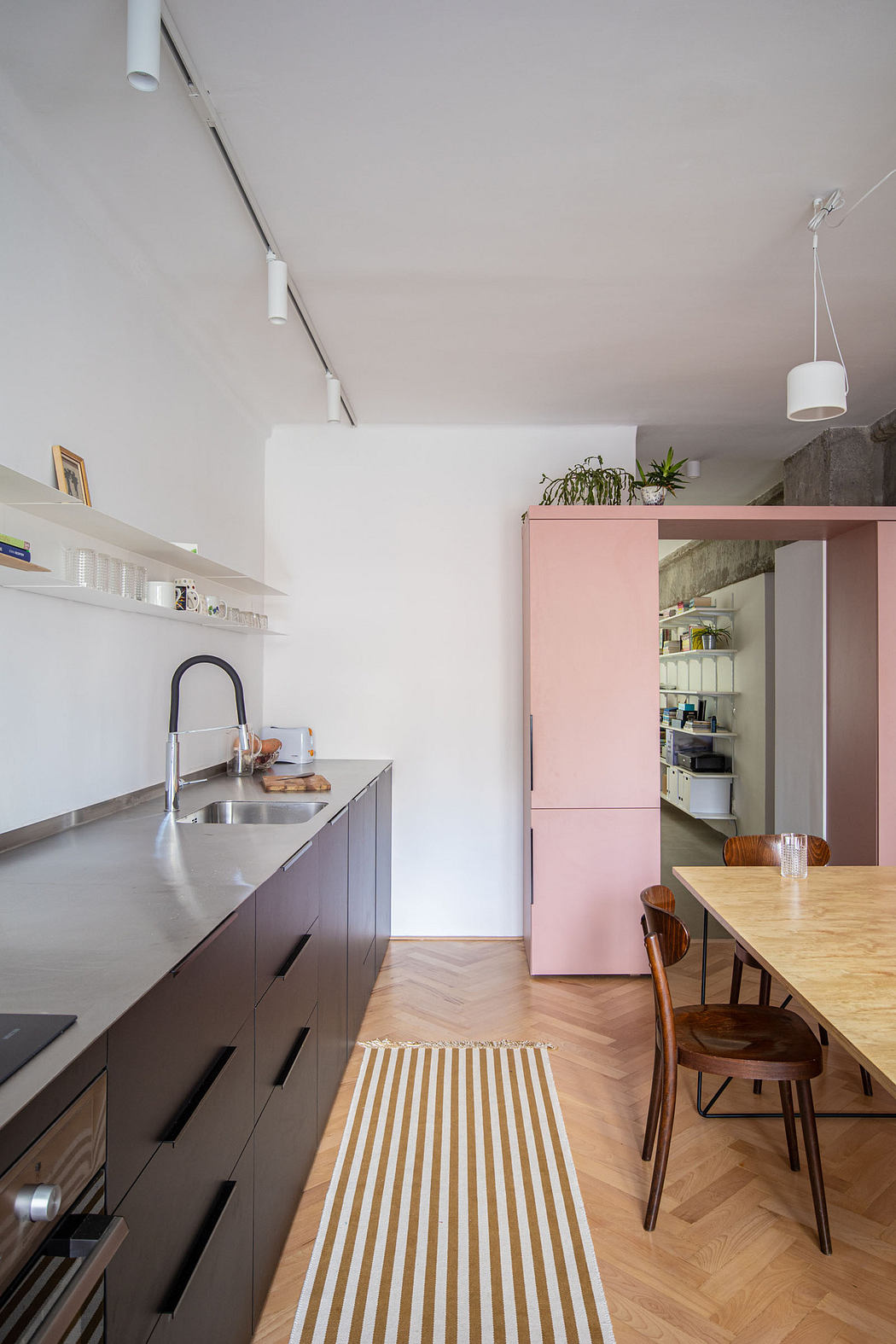 Modern kitchen interior with pink cabinets and wooden dining area.