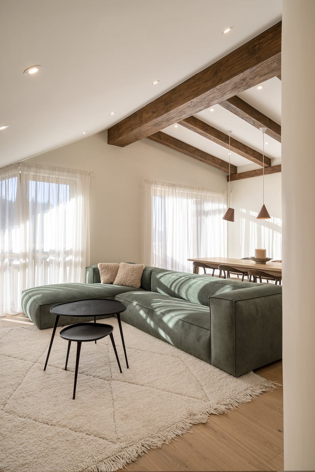 Modern living room with a green sofa, wooden beams, and pendant lighting.