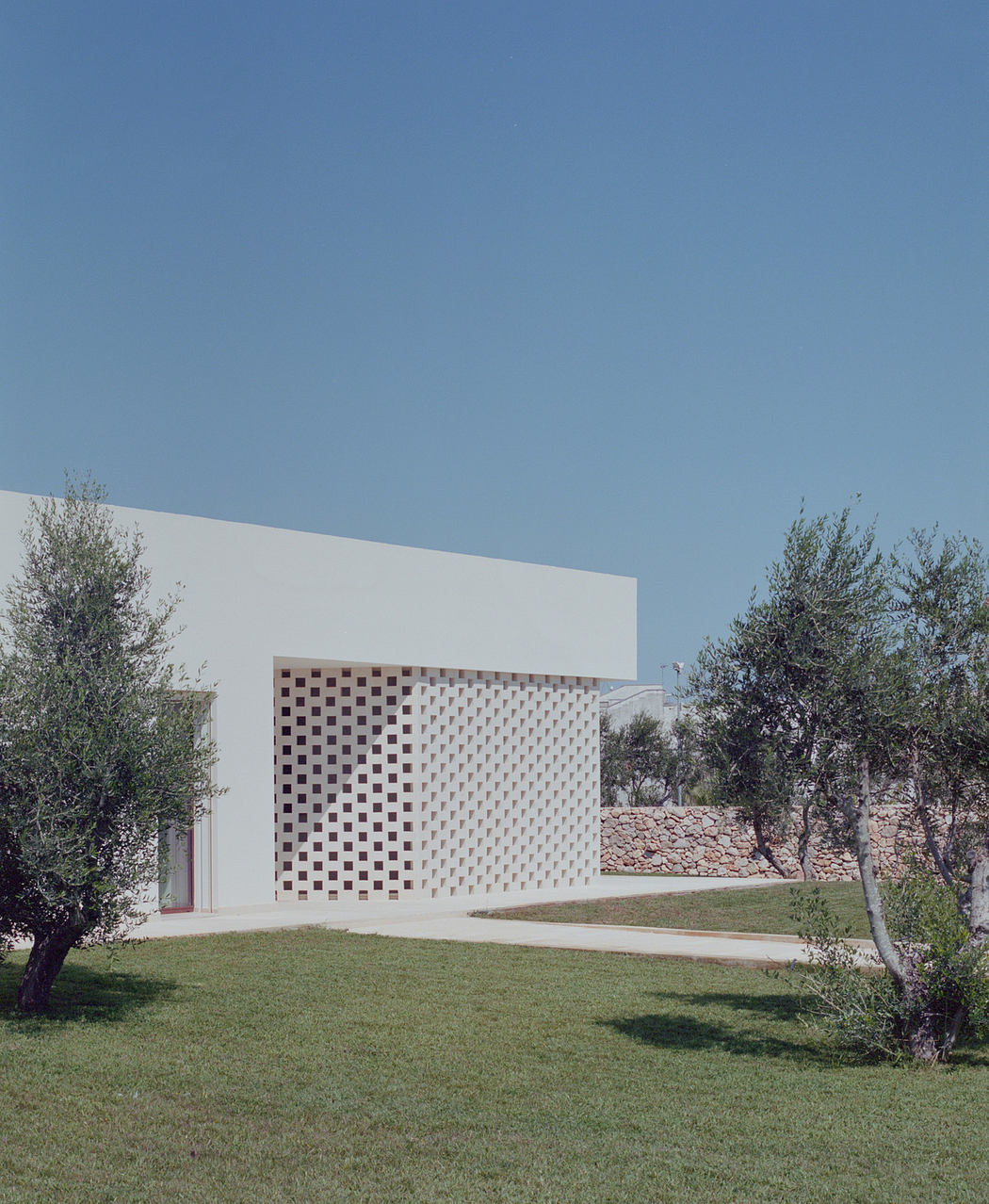 Modern white building with geometric facade and olive trees.