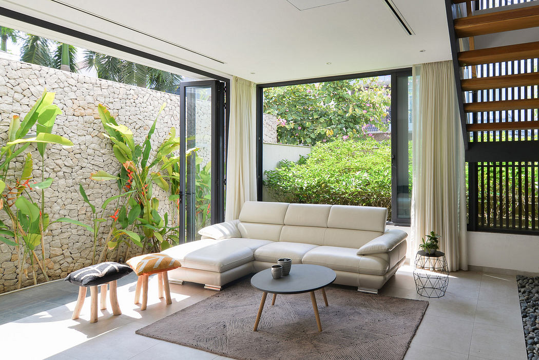 Modern living room with a white sofa, glass walls, and lush garden view.