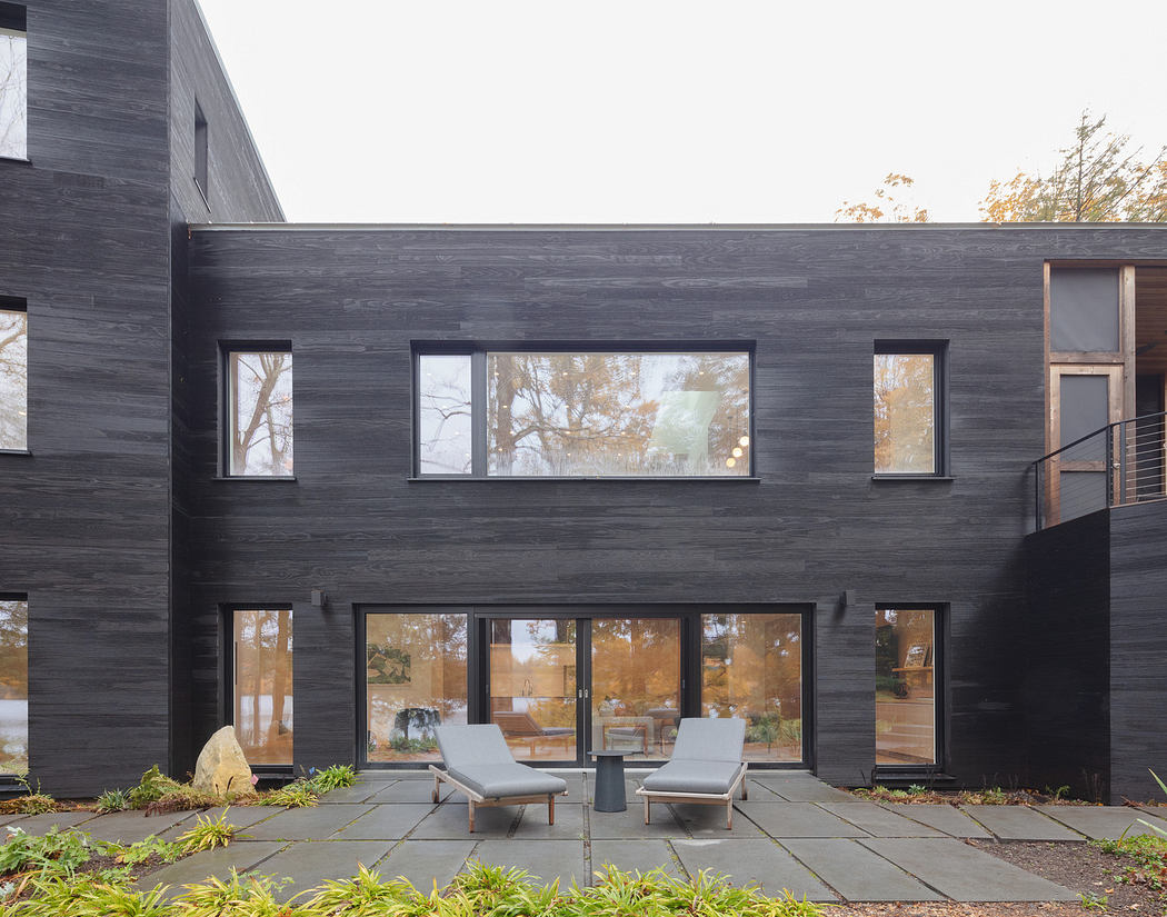 Modern black exterior of a house with large windows and outdoor seating area.