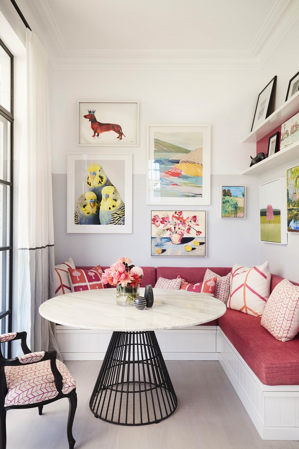 Bright dining nook with pink cushions, white table, art wall, and pattern