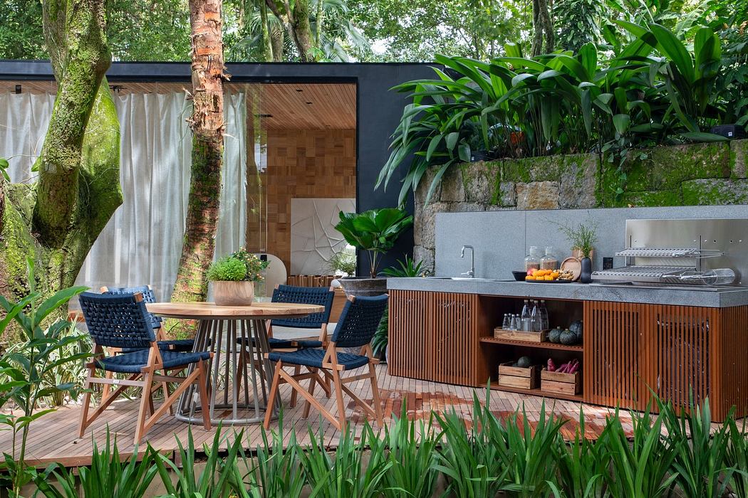 Modern outdoor patio with dining area and kitchenette surrounded by lush greenery.