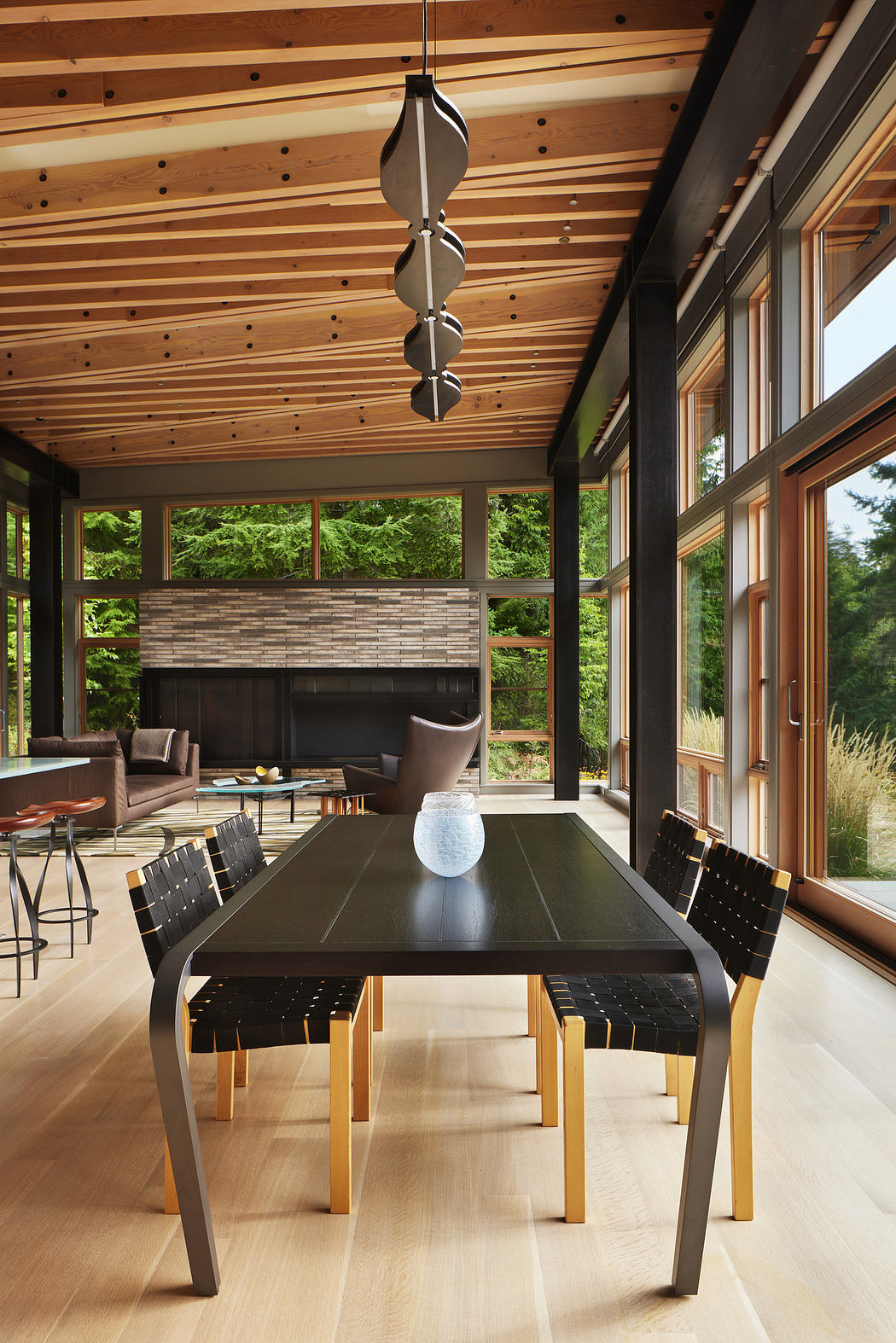 Modern dining room with wooden ceiling, large windows, and a sleek table.