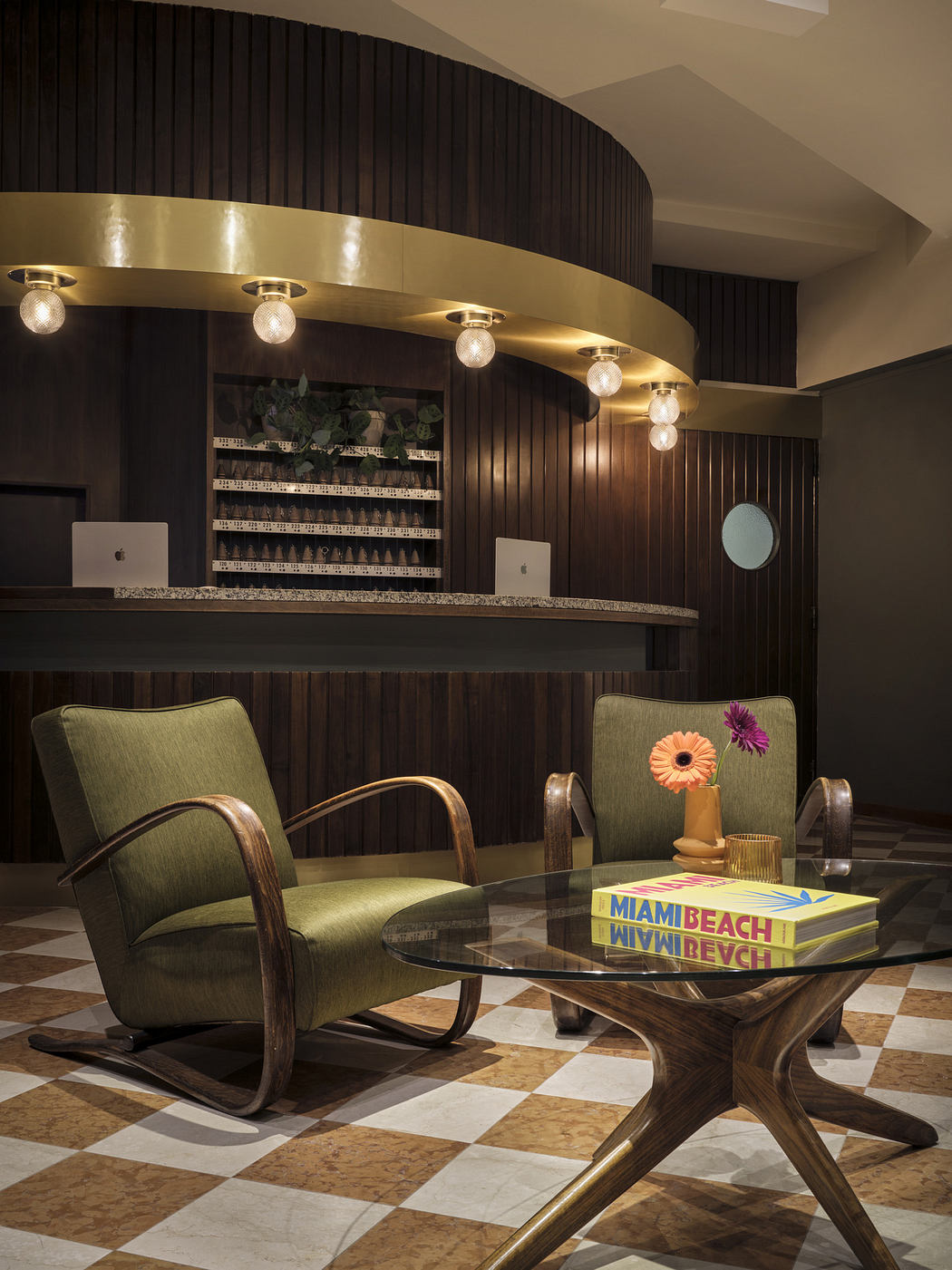Modern hotel lobby with circular reception desk, retro chairs, and checkered floor.